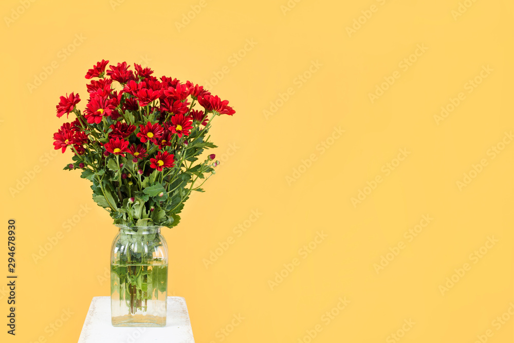Obraz premium Spring red flowers with green leaves in a vase on yellow background. Flower background. Add your text.