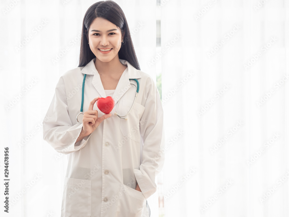 Portrait of a happy woman doctor standing and holding a red heart. Beautiful doctor smiling in a hospital or clinic. Portrait of a happy woman doctor standing and holding a red heart. Beautiful doctor smiling in a hospital or clinic.