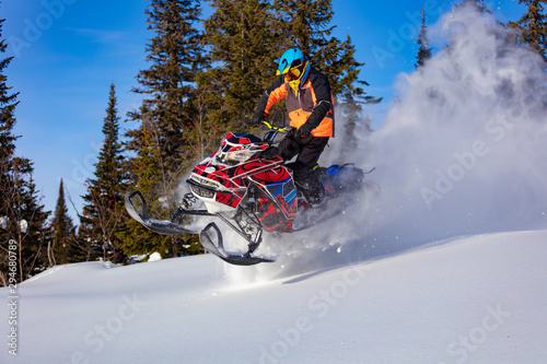 A man is riding snowmobile in mountains. Beautiful morning light. jump on a snow bike. pilot on a sports snowmobile in a mountain forest. The concept of skidooking. Lifestyle is active in winter sport © Wlad Go