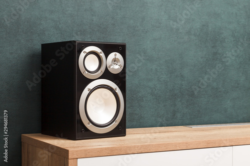 Single modern black audio speaker in interior on wooden desk near the wall photo