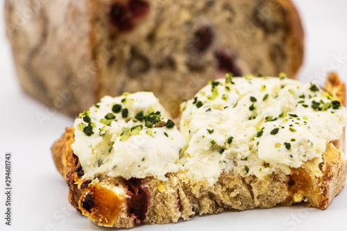 Tartine de fromage de chèvre frais aux fines herbes ail et échalotes ciselés sur une tranche de pain aux céréales et fruits secs arrière plan avec la miche de pain complete- isolé fond blanc studio