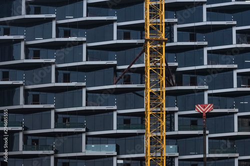 Detail of a construction crane against the background of the glass facade of a beautiful skyscraper. Abstract background with copy space