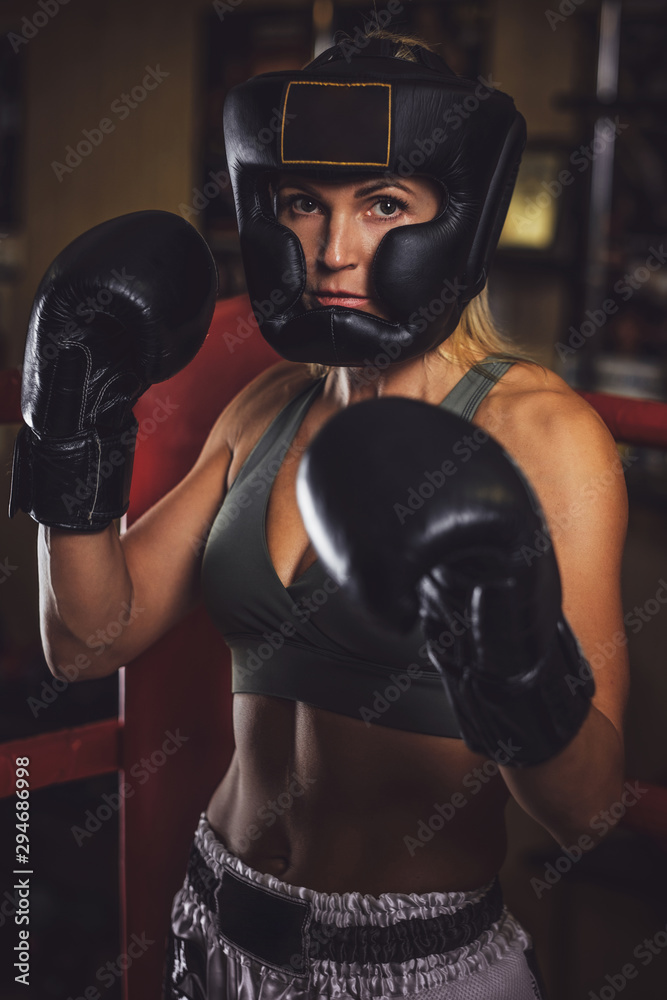 Serious young woman in protective helmet and boxing gloves with many cups at background. Serious young woman in protective helmet and boxing gloves with many cups at background.