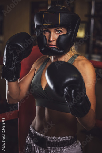 Serious young woman in protective helmet and boxing gloves with many cups at background.