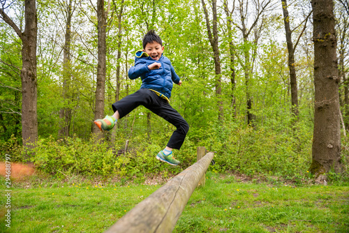 Boy jump and play across wooden trunk in forest photo