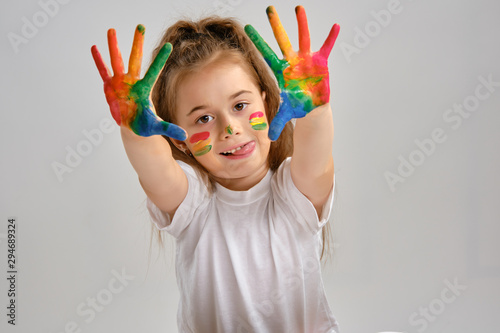Little girl in white t-shirt is posing standing isolated on white and showing her painted hands, face. Art studio. Close-up.