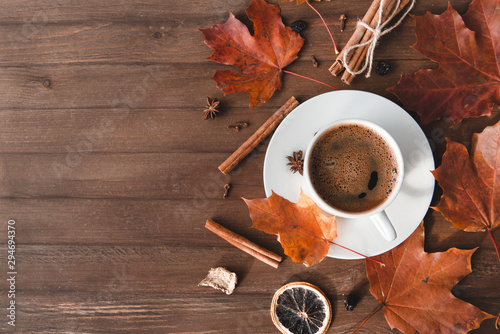 Cup of coffee with black coffee in a saucer on a wooden background, cinnamon,   red fallen autumn leaves, flat lay