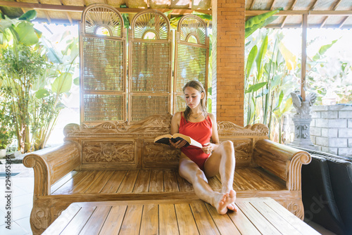Woman wearing swimsuit reading book on wooden sofa photo
