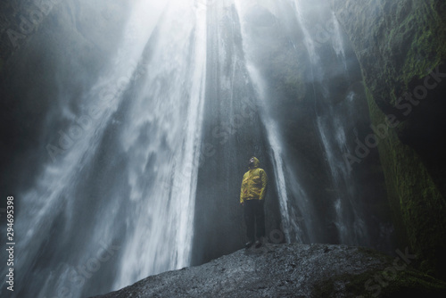 Man wearing yellow raincoat by Seljalandsfoss waterfall in Iceland