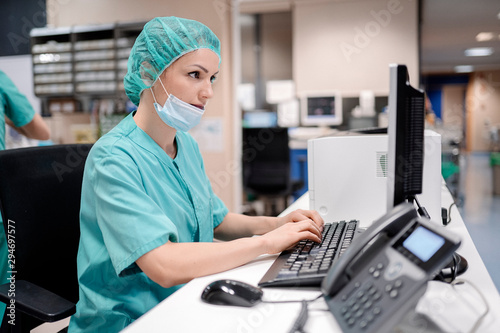Female doctor in uniform and mask using computer at table