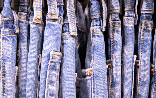 Several pairs of blue jeans on hanger, close up photo. Jeans size row. Tie Dye jeans clothes photo. Everyday wear on hanger in store