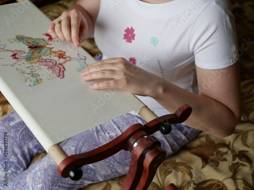 a young woman with beautiful hair in a white t-shirt embroiders colorful butterflies on a special wooden machine. Multicolored floss on a white canvas.