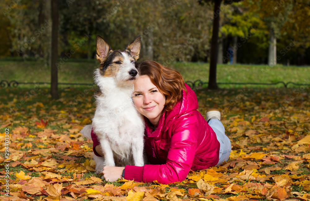 Beautiful girl is hugging love her dog and lying in autumn park on colorful yellow leaves, looking at camera and smiling. People love their pets concept. Young woman walking with her dog. Golden fall. Beautiful girl is hugging love her dog and lying in autumn park on colorful yellow leaves, looking at camera and smiling. People love their pets concept. Young woman walking with her dog. Golden fall.