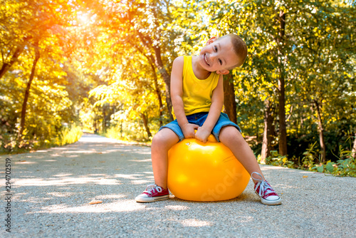 Adorable little smiling boy playing and jumping with hopper ball in park photo