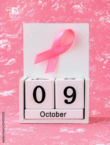 Pink ribbon of breast cancer awareness on a white wooden perpetual calendar with date 09 october. International breast cancer awareness month. photo