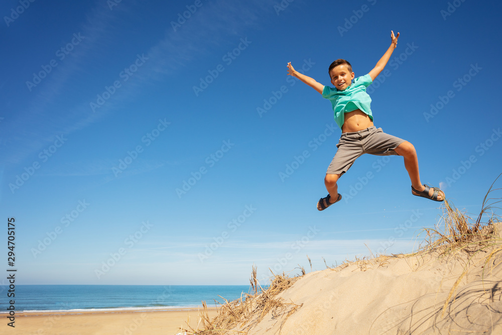 Happy boy jump high on the sand dune raising hands