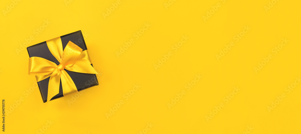 Black gift box with bow on yellow background. - obrazy, fototapety, plakaty 
