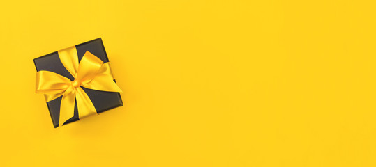 Black gift box with bow on yellow background.