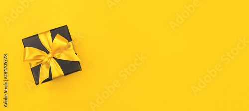 Black gift box with bow on yellow background. photo