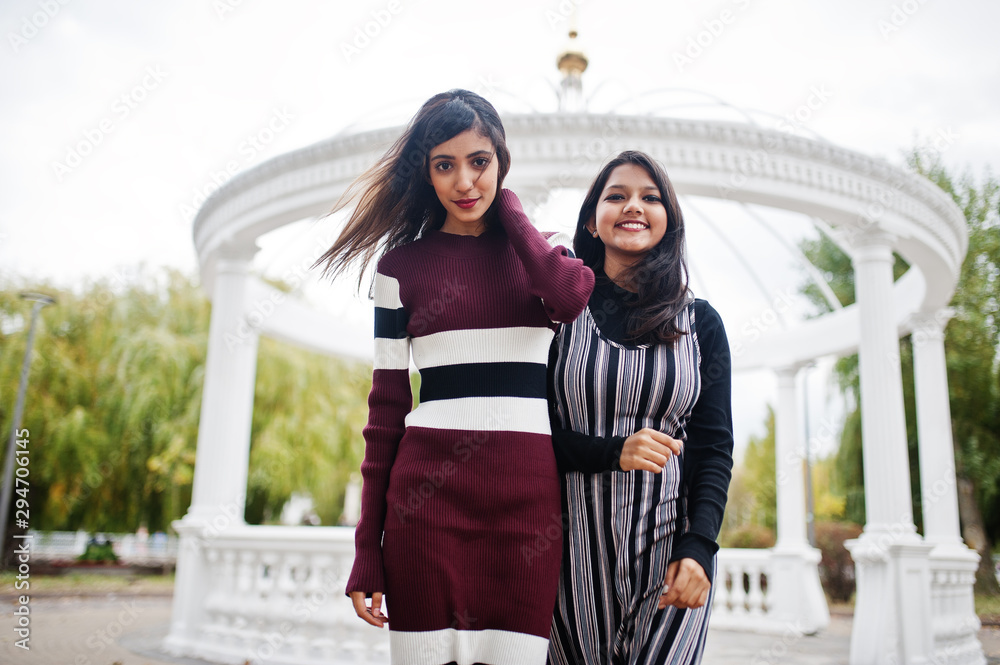 Portrait of two young beautiful indian or south asian teenage girls in dress background white temple arch.