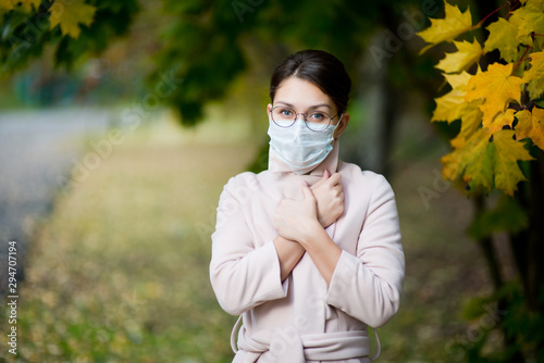 a woman in a medical mask closes her coat collar tightly on an autumn day
