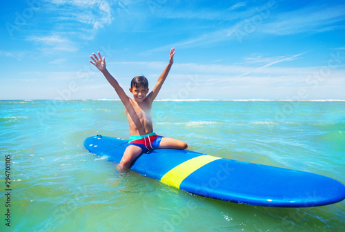 Little boy sit on surfboard with lifted hands up