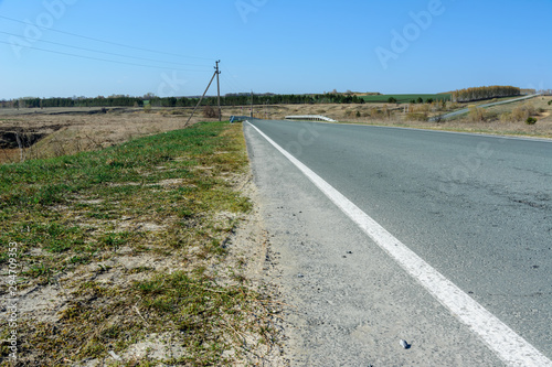 A winding highway stretching into the distance against the backdrop of a beautiful spring landscape, fields, meadows, forests and hills. Road stripes on asphalt. © Evgeniy