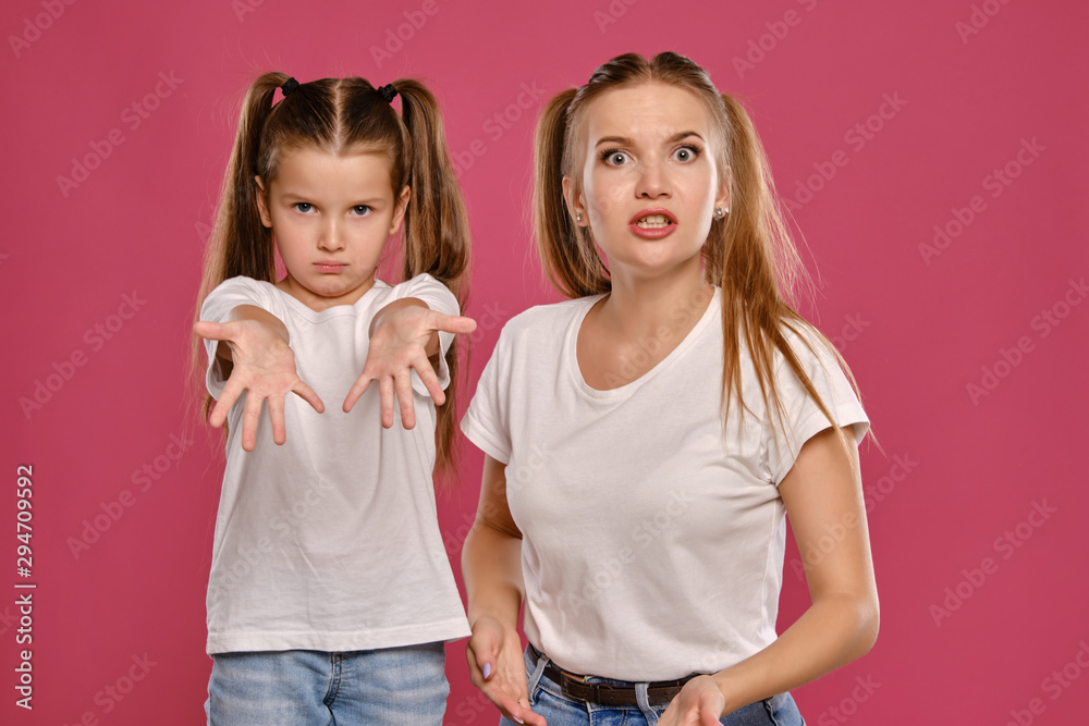 Mom and daughter with a funny ponytails, dressed in white t-shirts and blue denim  jeans are posing against a pink studio background. Close-up shot. Stock  Photo | Adobe Stock