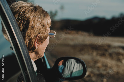 A old woman with her head out the window enjoying a scenic drive
