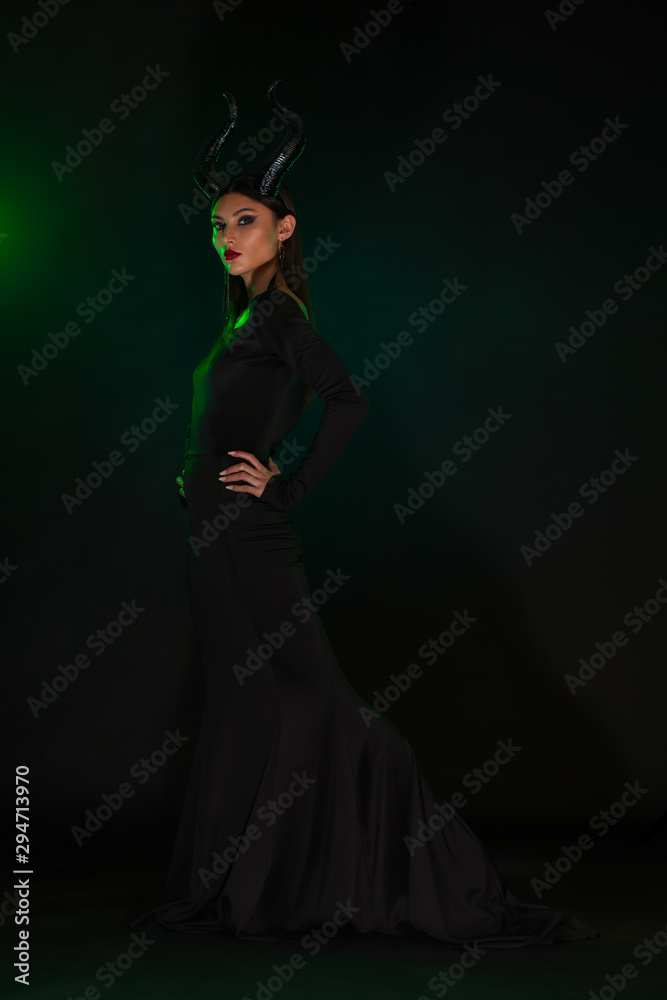 Concept of Halloween and fantasy horror. Cosplay on Maleficent demonic - starring. Face of beautiful woman from a fairytale with horns in green smoke. Beautiful girl dressed up as devil. Concept of Halloween and fantasy horror. Cosplay on Maleficent demonic - starring. Face of beautiful woman from a fairytale with horns in green smoke. Beautiful girl dressed up as devil.