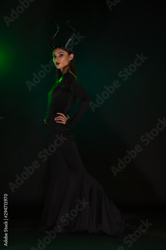 Concept of Halloween and fantasy horror. Cosplay on Maleficent demonic - starring. Face of beautiful woman from a fairytale with horns in green smoke. Beautiful girl dressed up as devil.