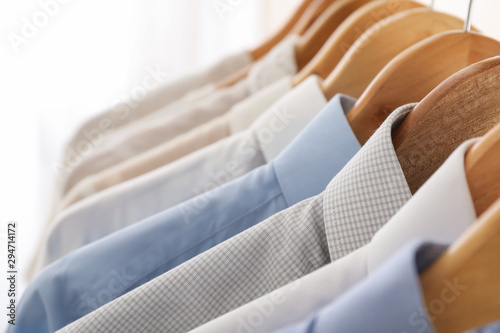 Hangers with shirts against light background, space for text