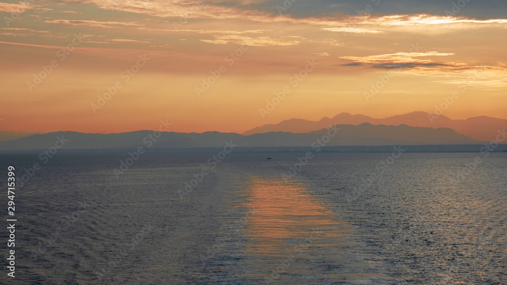 Nature in twilight period which including of sunrise over the blue water in the morning. Beautiful colorful landscape with boats, sea and purple sky. Golden light go through the cloud to the mountain 