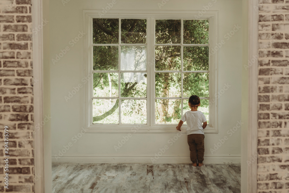 Toddler boy looking out window at trees in natural light studio Toddler boy looking out window at trees in natural light studio