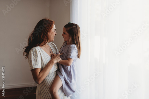 Side view of young mother holding young daughter and smiling at her photo