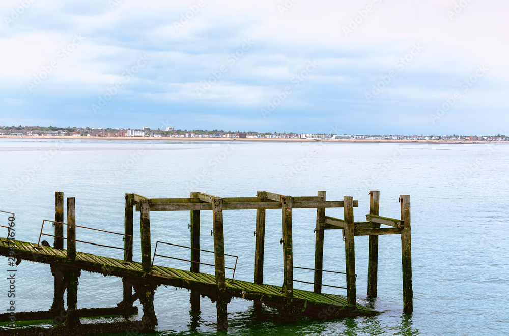 old withered wooden pier standing in sea water with city outline and beach in background old withered wooden pier standing in sea water with city outline and beach in background
