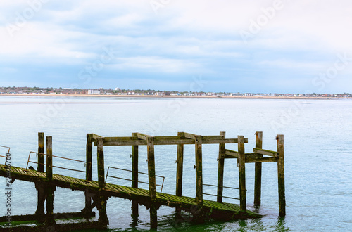 old withered wooden pier standing in sea water with city outline and beach in background