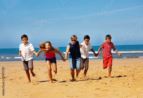 Fun happy kids group run holding hands on a beach