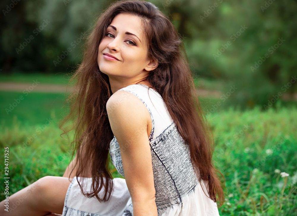 Beautiful calm relaxing young woman with long hair sitting on the grass and looking up on summer green background. Closeup Beautiful calm relaxing young woman with long hair sitting on the grass and looking up on summer green background. Closeup