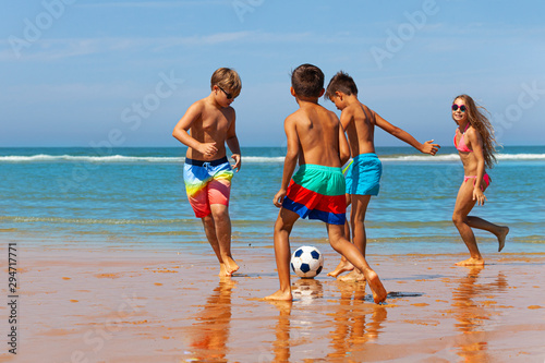 Children play soccer on the sand beach near water