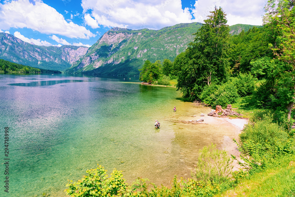 Scenery of Bohinj Lake in Slovenia. People fishing and Nature in Slovenija. View of green forest and blue water. Beautiful landscape in summer. Alpine Travel destination. Julian Alps mountains