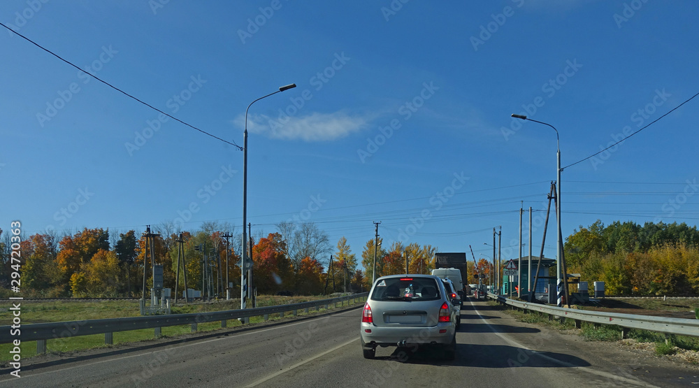 The line of cars standing on the railway crossing waiting for the passage of the train on an autumn day