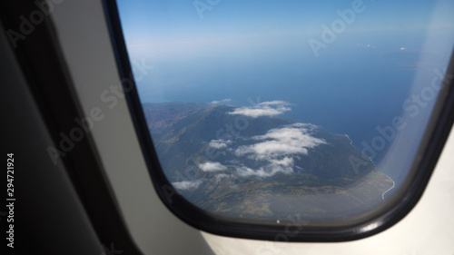 aircraft porthole window with blue sea or ocean in it and small tropical islands. Looking through window aircraft during flight