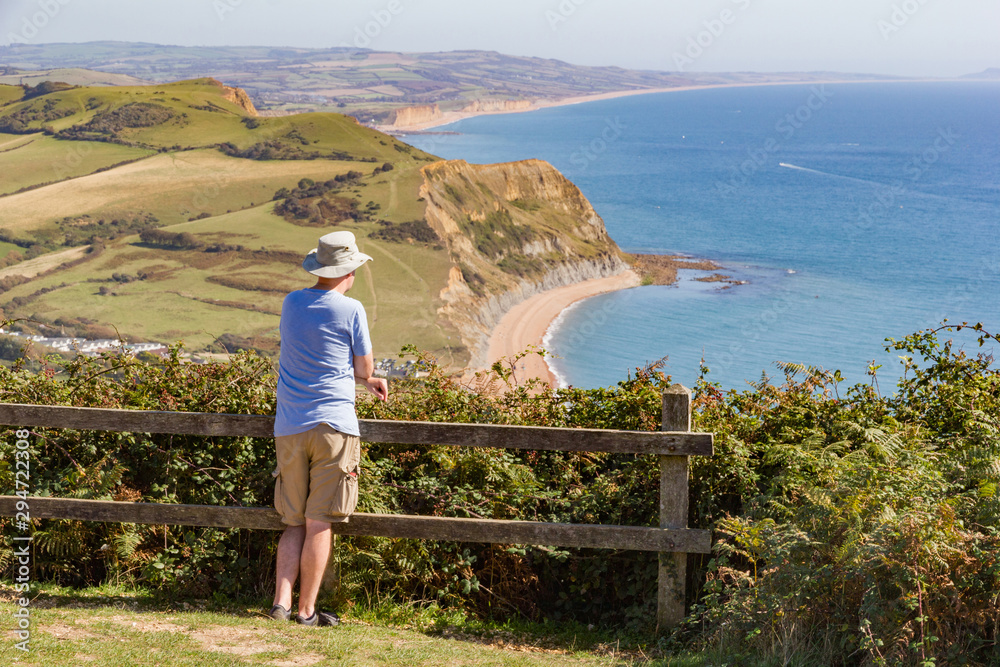 Person takes in the view out to sea from the top of Golden Cap in West Dorset, England, with background view of Bridport sandstone cliffs and Chesil beach