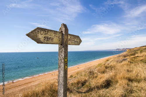 Bild auf Leinwand A weather worn wooden sign points the way of the west Dorset coast path along th