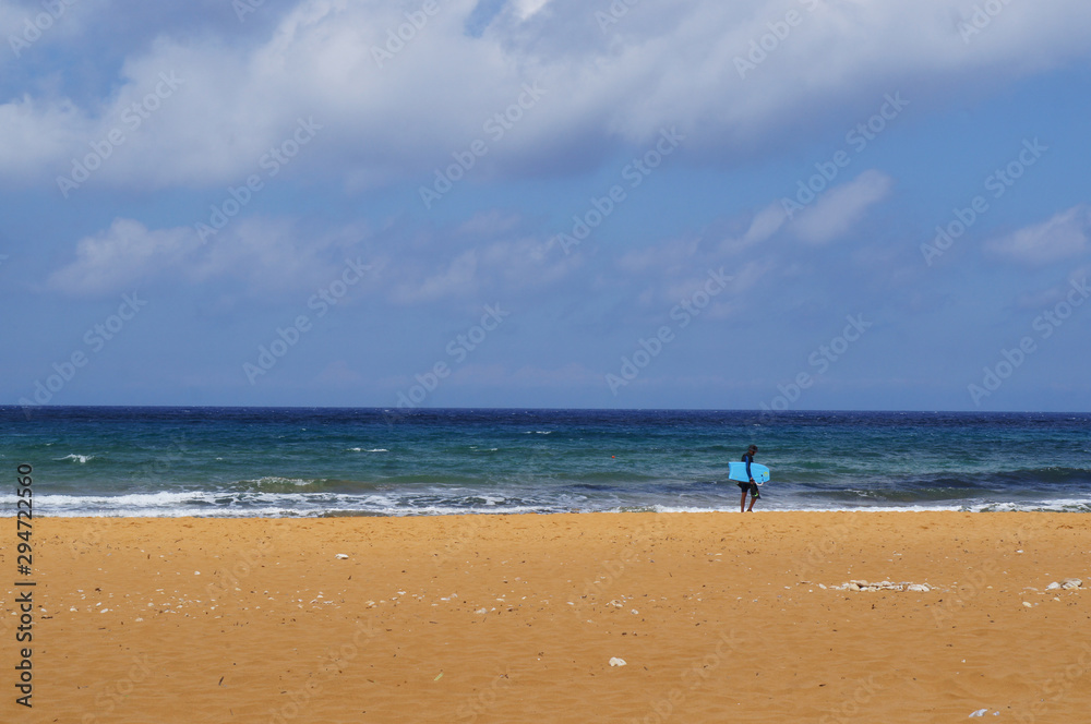 Lonely surfer on red sandy beach in Ramla Bay, Gozo, Malta