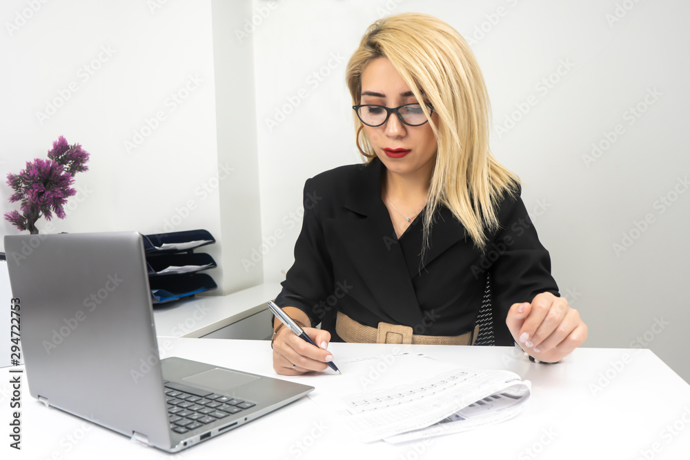 Business woman using calculator and writing make note with calculate. Woman working at office with laptop and documents on his desk Business woman using calculator and writing make note with calculate. Woman working at office with laptop and documents on his desk