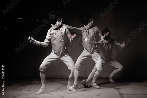 Fencer in white outfit is performing fight. Multi Exposure, freeze light, dark background 