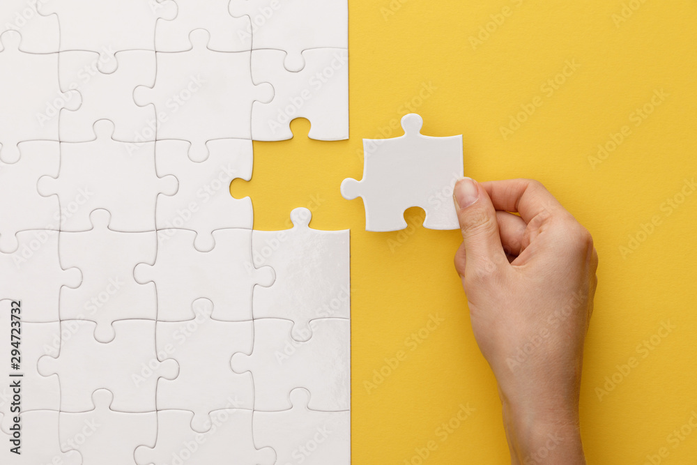 cropped view of woman putting piece of white jigsaw puzzle on yellow background - obrazy, fototapety, plakaty 