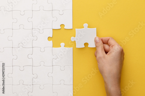 cropped view of woman putting piece of white jigsaw puzzle on yellow background photo